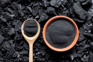 A finely crushed black powder in a wooden spoon and orange bowl.